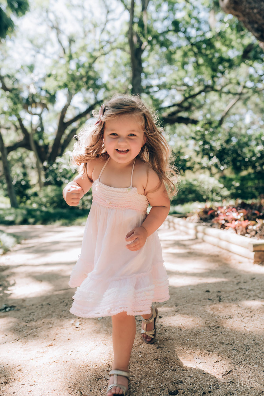 toddler in a pink dress running under shade trees