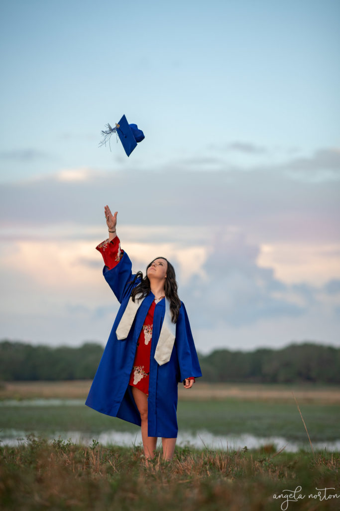 senior tossing up cap in front of lake during blue hour